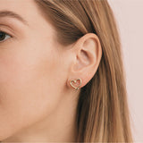Heart-shaped gold earring worn by a woman with brown hair.