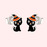A pair of silver-colored hypoallergenic earrings featuring a black cat with an orange and black witch's hat design.