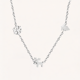 Silver necklace with Christmas charms on a light pink background.