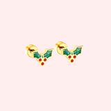 Gold earrings with green holly leaves and red berries on a light pink background