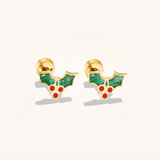 Gold earrings with green holly leaves and red berries on a light background