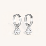 Silver hoop earrings with snowflake charms on a pink background.