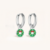 Silver hoop earrings with green wreath charms featuring red bows on a light background