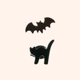 An earring set containing a bat and a black cat on a light pink background.