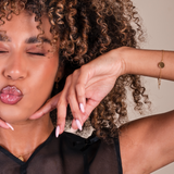 Woman with curly hair and pink lipstick showing a bracelet against a neutral background