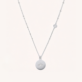 Silver necklace with a round pendant on a white background