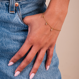 Hand wearing a gold bracelet with blue jeans in the background