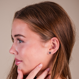 Closeup of a girl wearing daisy stud hypoallergenic earrings in silver on a beige background.
