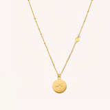 Gold necklace with circular pendant on a light beige background