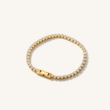 A gold cubic zirconia tennis bracelet on a beige background.