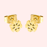 A pair of gold snowflake stud earrings on a light pink background.