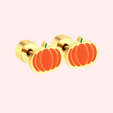 A gold pair of orange pumpkin earrings on a light pink background.