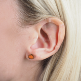 Close-up of a girl wearing a gold pumpkin-shaped earring with blonde hair.