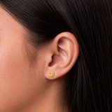 A close-up of a girl's ear wearing a small circular yellow and red smiley face stud earring.