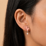 A close-up of a model's ear wearing a silver butterfly stud earring with pink inlay and a dangling pearl.