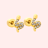 Pair of gold serpent earrings with crystal gems on a light pink background