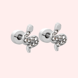 Pair of silver serpent earrings with crystal gems on a light pink background