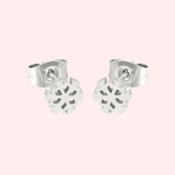 A pair of silver snowflake stud earrings on a light pink background.