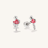 A pair of silver stud earrings shaped like dancing ballerinas holding a red heart-shaped cluster of small clear stones, shown on a clean off-white background.