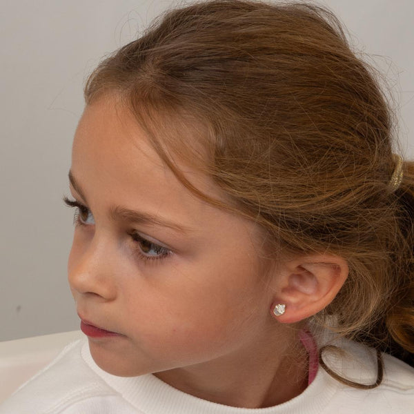 Young girl wearing a small cupcake earring against a plain background