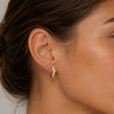Close-up of model wearing Gold Wave Crystal Huggie Earrings with a curved wave design set with clear cubic zirconia stones