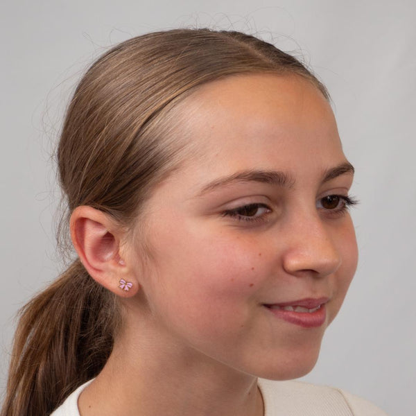 Girl with a ponytail wearing pink bow earrings against a plain background