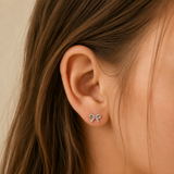 A lifestyle image of a girl wearing silver bow earrings with a pink gem.
