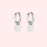 Silver hoop earrings with snowflake charms on a pink background.