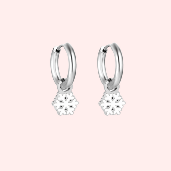 Silver hoop earrings with snowflake charms on a pink background.
