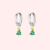 Silver hoop earrings with green Christmas tree charms on a light pink background