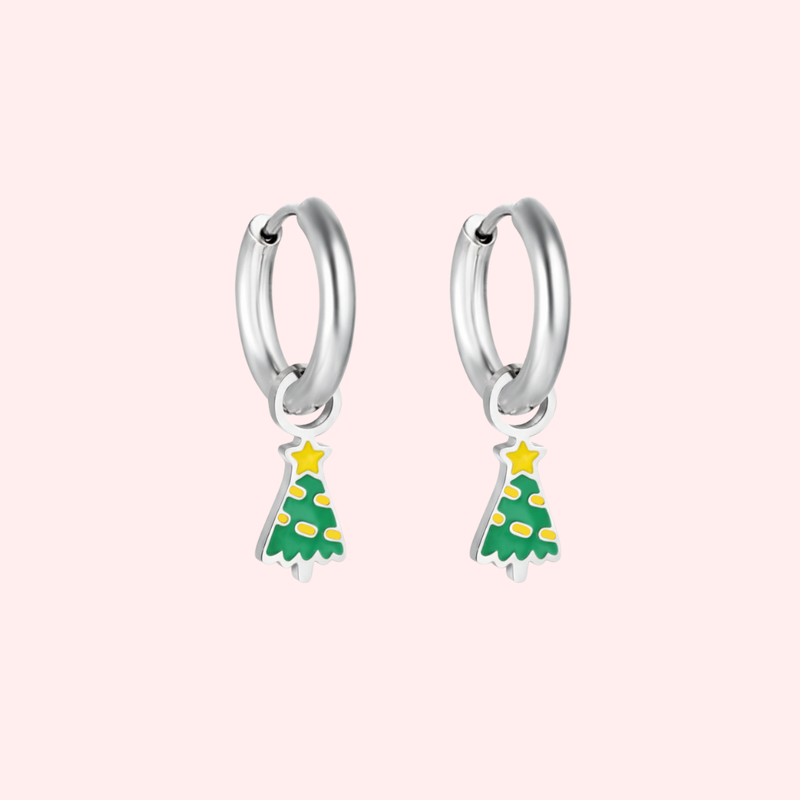 Silver hoop earrings with green Christmas tree charms on a light pink background