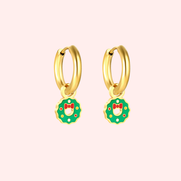 Gold hoop earrings with green wreath charms featuring red bows on a light pink background