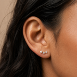 A lady wearing gold stud earrings with three crystals. 