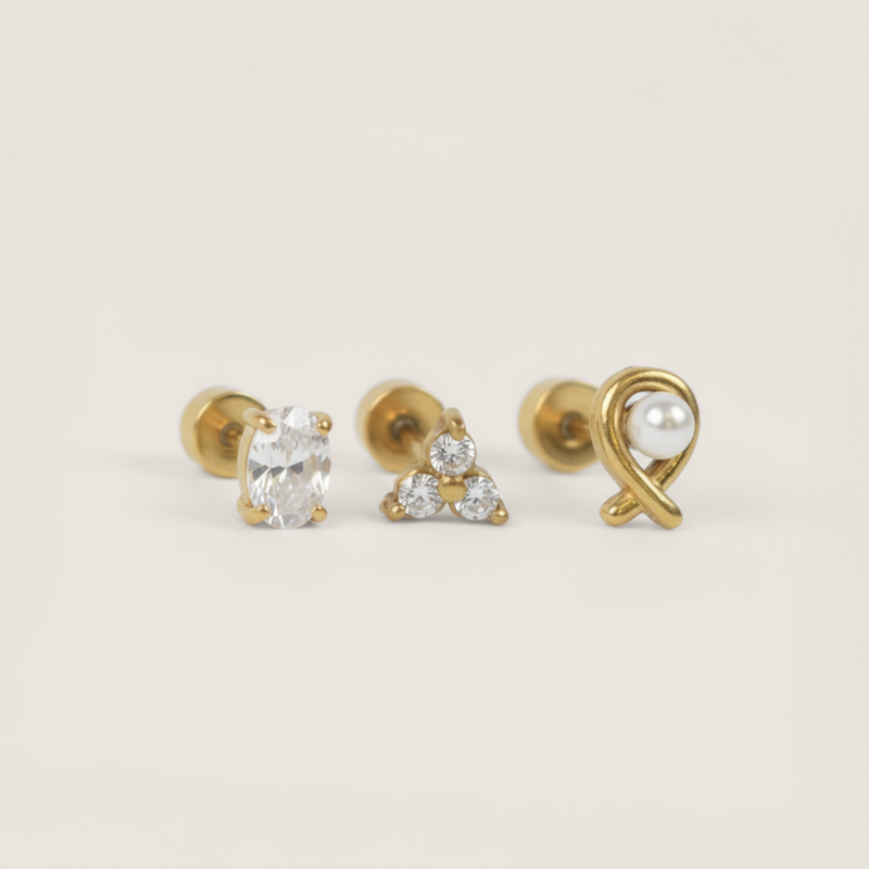 Three gold earrings with gemstones on a light beige background