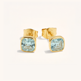 Gold earrings with square blue gemstones on a white background