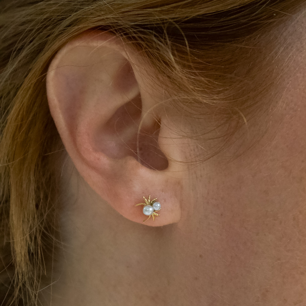 Close-up of a girl wearing a gold spider earring with pearls.