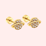Gold planet-shaped earrings with embedded crystals on a light pink background.
