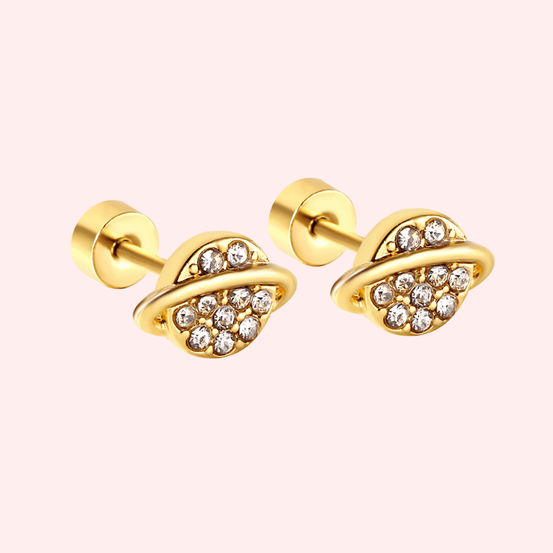 Gold planet-shaped earrings with embedded crystals on a light pink background.