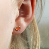 Close-up of a girl wearing a silver  pumpkin-shaped earring with blonde hair.