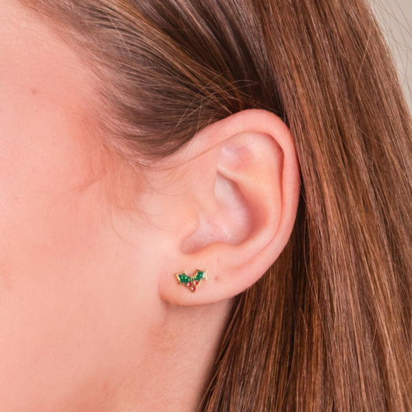 Close-up of a girl wearing green and gold holly Christmas earrings with a blurred background.