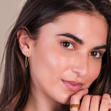 Close-up of a woman wearing gold earrings and a ring on a neutral background