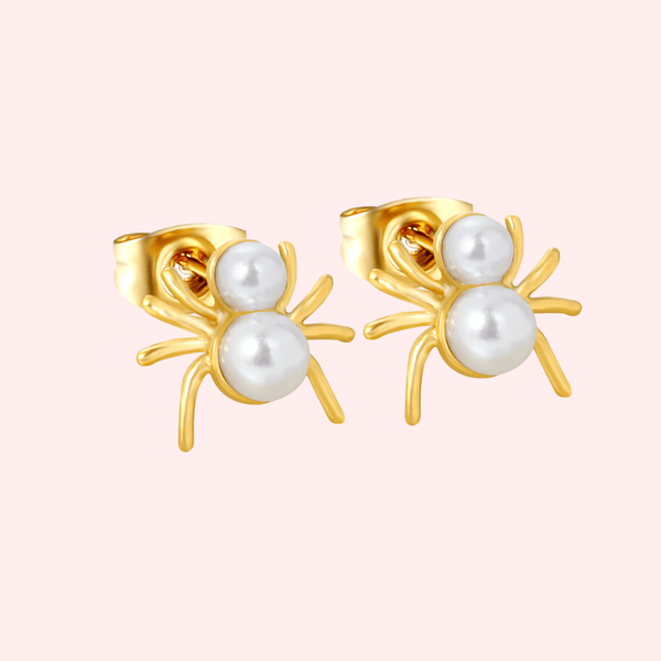 Gold spider-shaped earrings with pearl centers on a light pink background