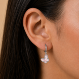 A close-up of a girl's ear wearing a delicate silver huggie hoop earring with a dangling butterfly-shaped charm set with light pink stones.