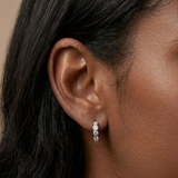 A woman wearing silver huggie earrings with cubic zirconias paved throughout them.