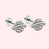 Silver planet-shaped earrings with embedded crystals on a light pink background.