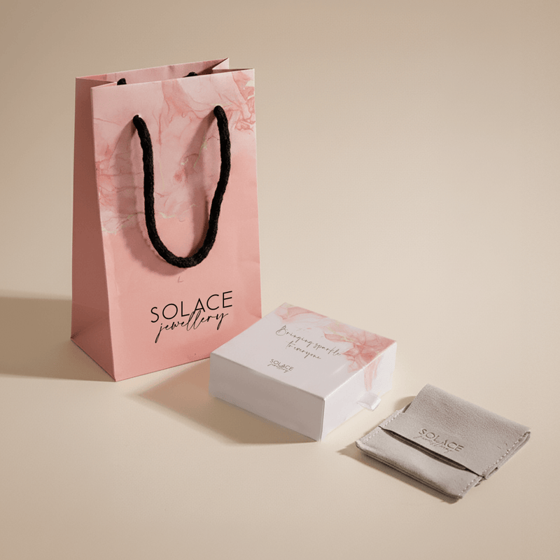 Solace jewellery packaging including a pink bag, white box, and gray pouch on a beige background.